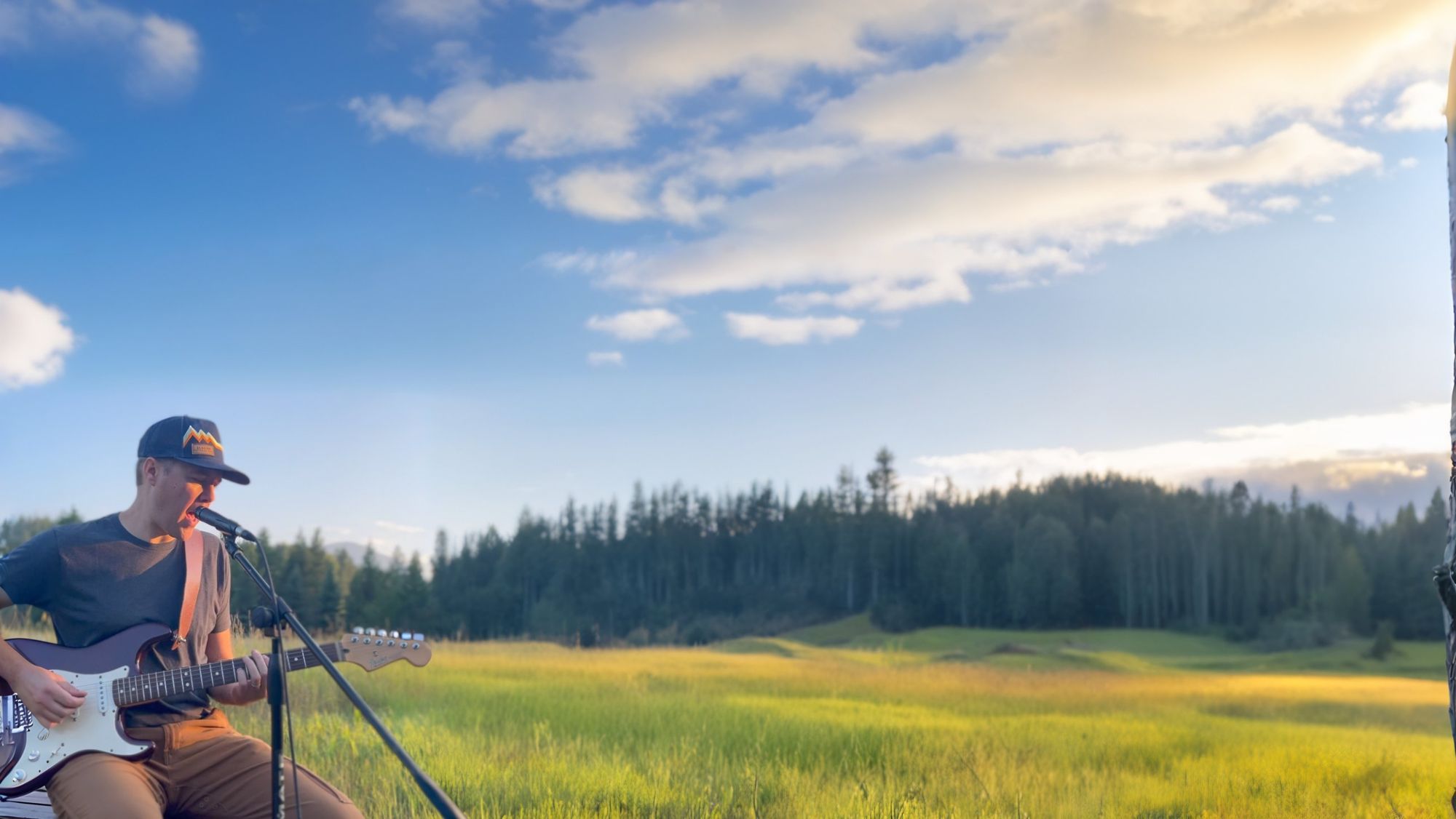 Playing an electric guitar and singing into a microphone in a mountain meadow at golden hour